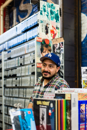 Miles Alva, 28, during his shift at Videotheque, a video store in South Pasadena. The television and cinema arts student says getting insured is not a priority and would rather deal with the penalty  (Photo by Heidi de Marco/KHN).