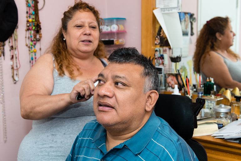 Frances Chuc brushes her husband’s hair.  Jorge Chuc has been paralyzed for more than 30 years and needs full-time care from his wife (Photo by Heidi de Marco/KHN).