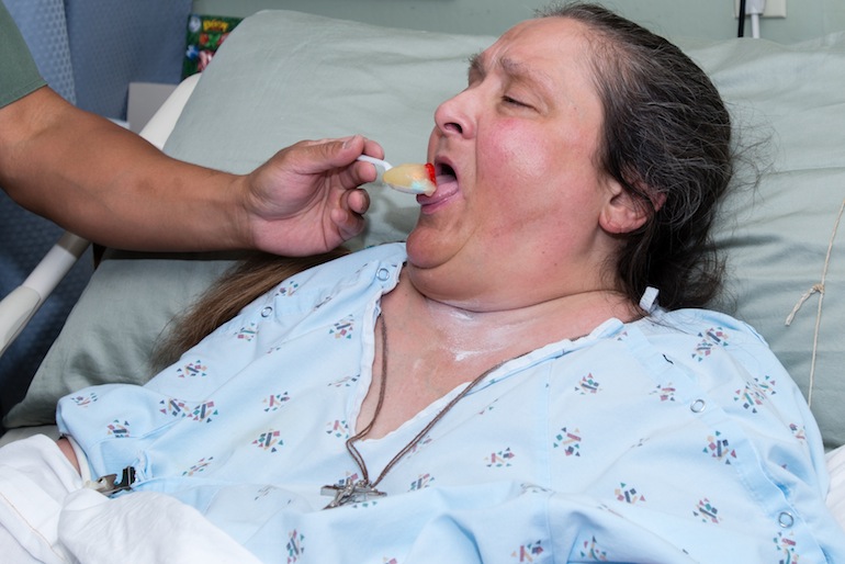 Toni Giusto, 54, takes a pill with her applesauce, administered by her night nurse (Photo by Heidi de Marco).