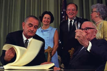 President Lyndon B. Johnson signed the bill creating Medicare and Medicaid at the library of former President Harry Truman, who was in attendance, on July 30, 1965. (Photo courtesy of Truman Library)