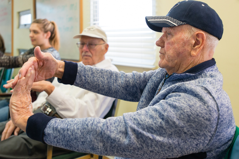 Tracy Williams, 80, stretches during the morning exercises at the WISE & Healthy Aging adult day service center. Williams, retired from the Air Force, said he enjoys when the college students visit the adult day service center visit. (Heidi de Marco/KHN)