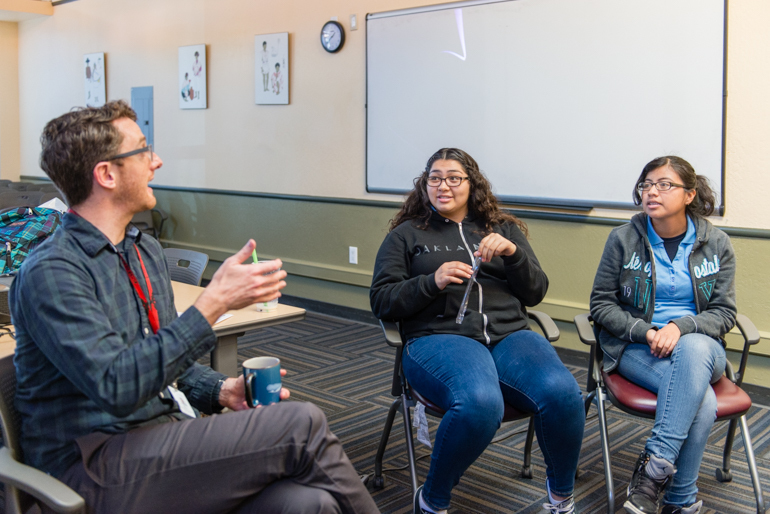 Eric Waters, coordinator for the behavioral health program at the Life Academy High School, leads a discussion with Fernanda May, 17, and Graciela Perez, 17, at La Clínica de la Raza in Oakland, Calif., on January 27, 2016. The program provides training in mental health first aid and places students in internships with mental health organizations. (Heidi de Marco/KHN)