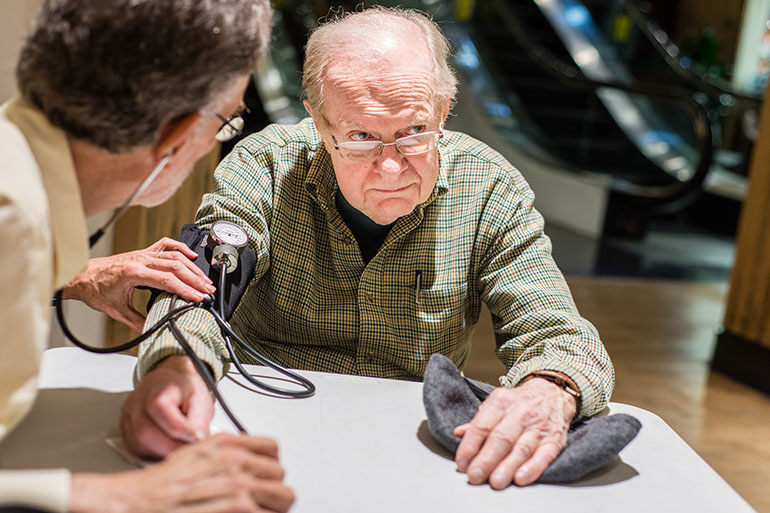 Dr. Aric Schichor checks Joe King's blood pressure at Mazza Gallerie in Washington, D.C., on Tuesday, March 15, 2016. Schichor is retired and volunteers his time at every mall walking session. (Heidi de Marco/KHN)