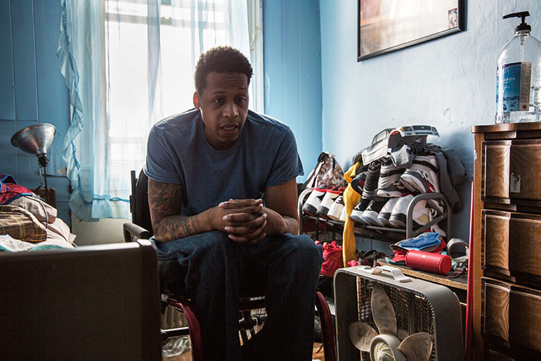 Vincent Berry, 28, who was paralyzed from a gunshot wound several years ago, lives with his grandmother in East Baltimore. Donnie Missouri, 58, a Johns Hopkins Hospital aide, is trying to help him find him stable, wheelchair-accessible housing. (Francis Ying/KHN)