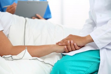 Friendly female doctor hands holding patient hand lying in bed for encouragement, empathy, cheering and support while medical examination. Bad news lessening, compassion, trust and ethics concept