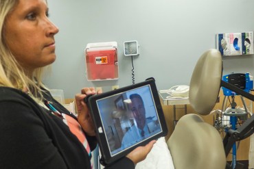 Thomas Milam, the interim director of psychiatry and behavioral health at Carilion Clinic, is based in Roanoke, Va. But if patients in Pearisburg need a consult, he will tele-conference in, appearing on a screen like the one held by Michelle Dowdy, the office manager at Giles’ family medicine clinic. (Shefali Luthra/KHN)