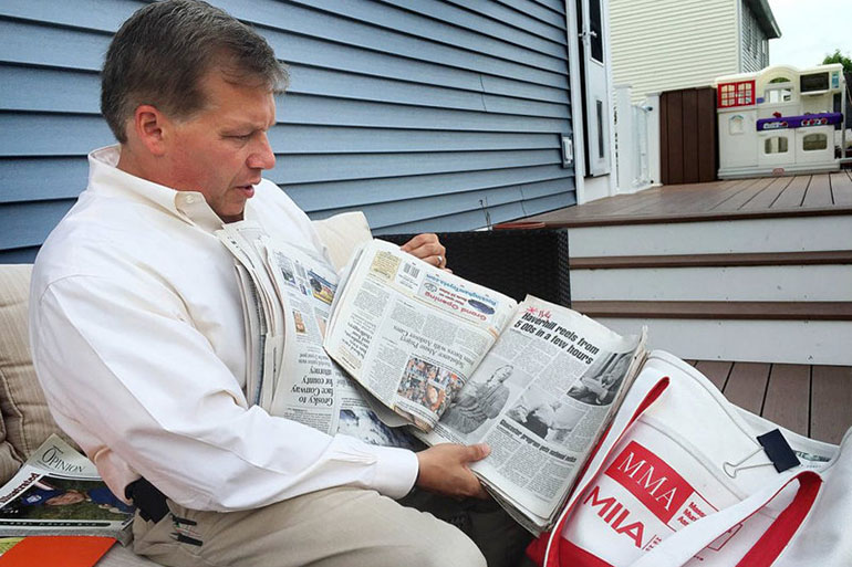 At his home in Haverhill, Mass., Colin LePage leafs through newspapers he shows to middle-schoolers to educate them about the dangers of drugs. (Martha Bebinger/WBUR)