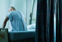 A man in a hospital gown sits on a hospital bed