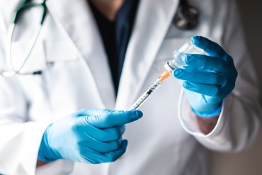 Doctor in white coat drawing vaccine into a syringe for injection.