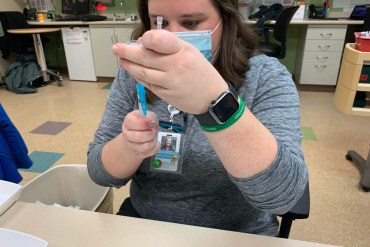 Beth Ann Wilmore checks a vaccine vial at her community health center