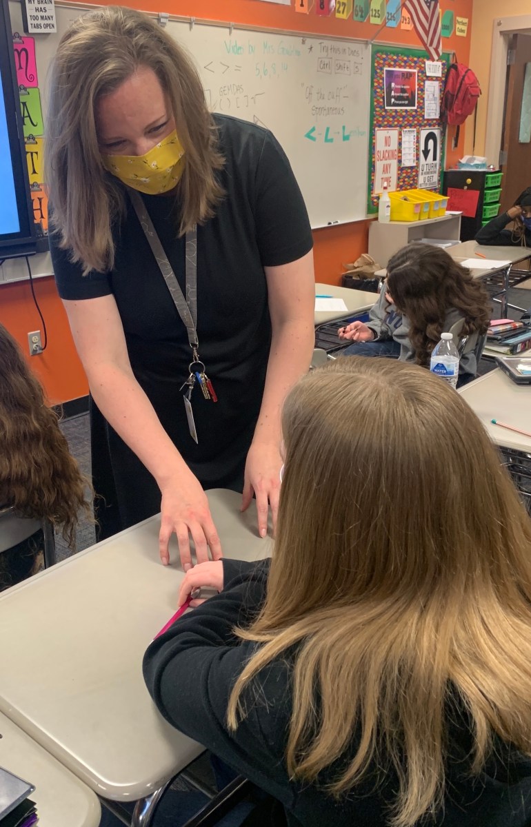 teacher wearing mask instructs seated child