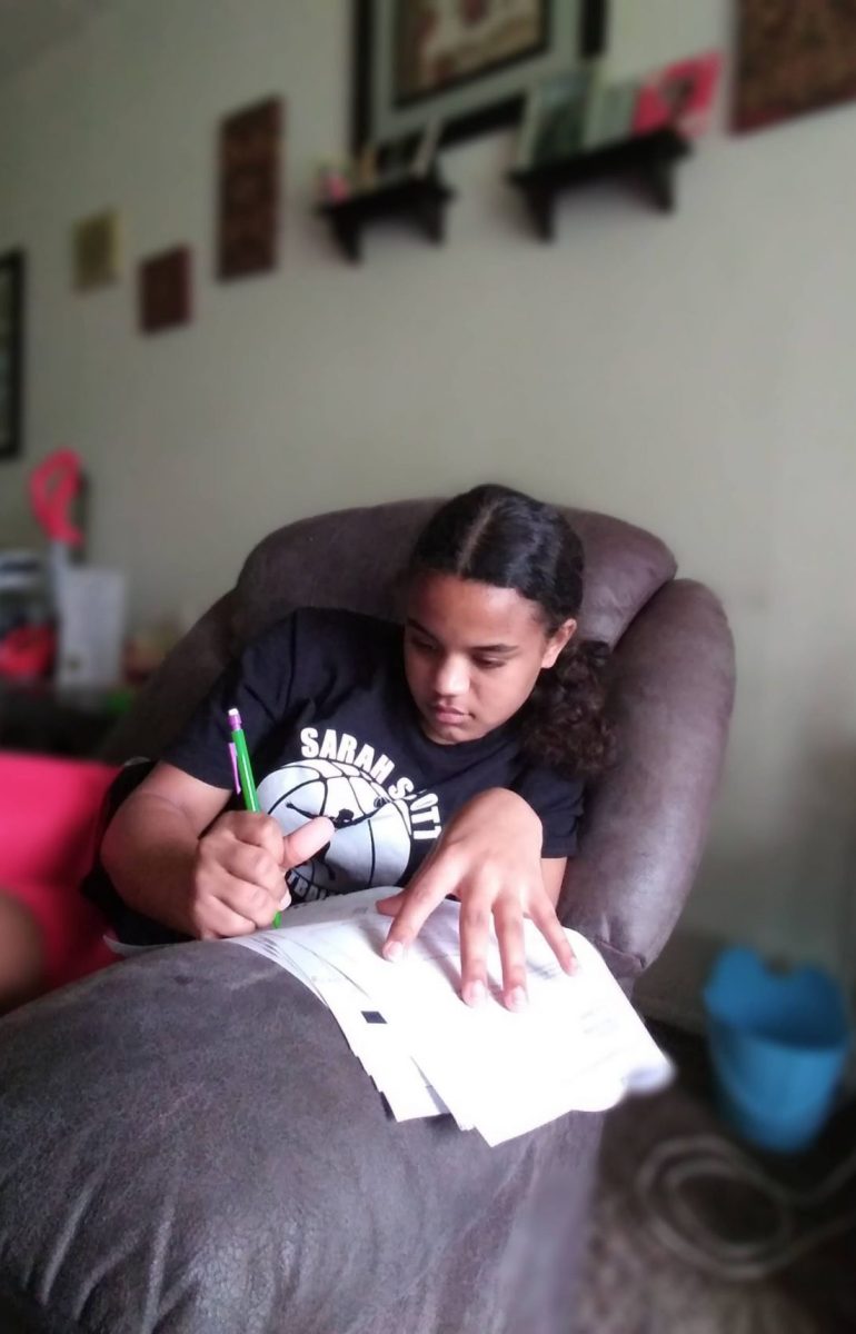 young girl writing while seated on couch with papers on the armrest and a pen in hand