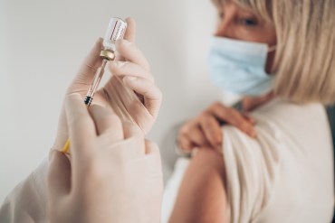 Female doctor giving a vaccine of mature woman at home.