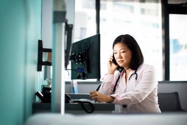 Female doctor using smart phone computer desk in clinic