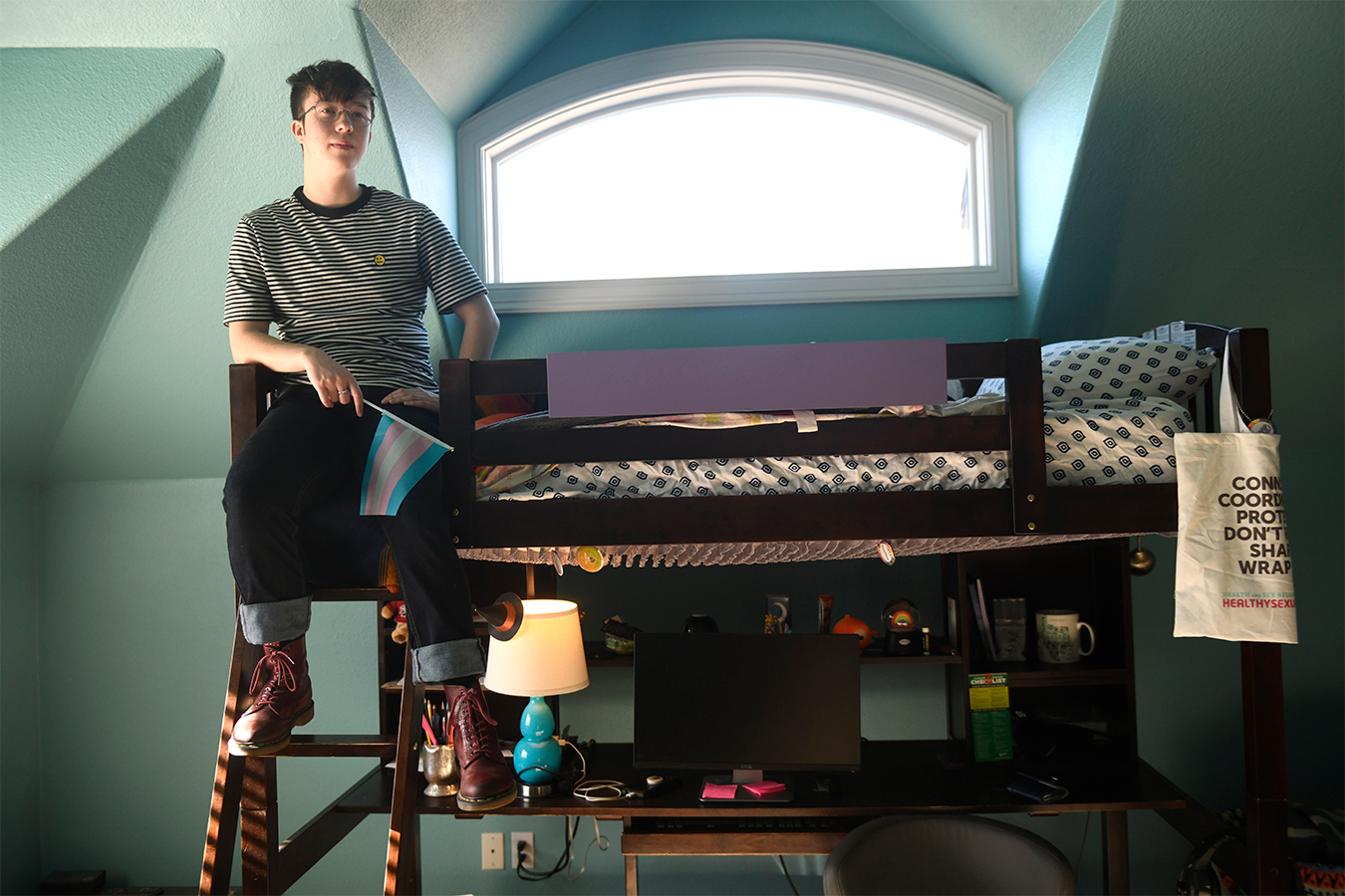 Charlie Apple holds a transgender pride flag while sitting on his bed.