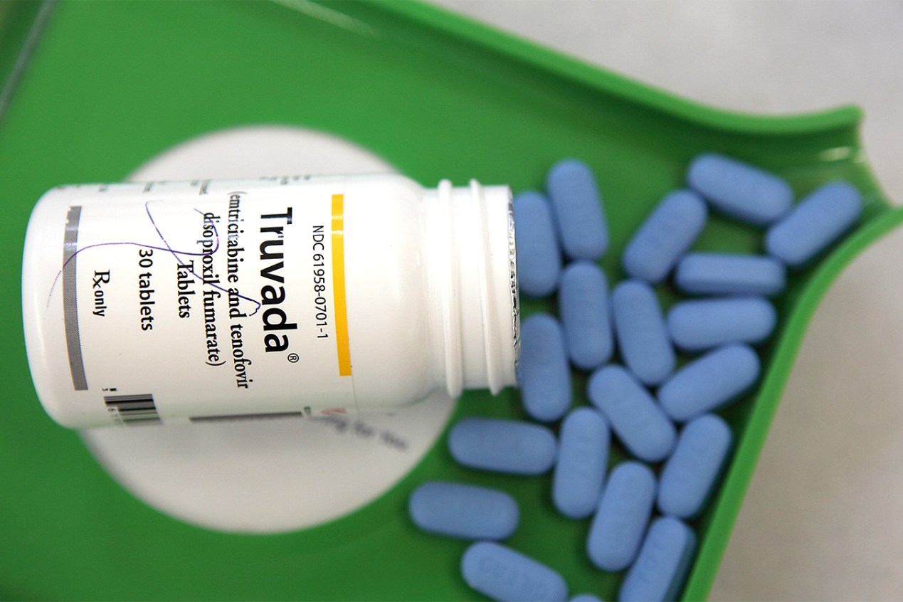 A bottle of Truvada, an HIV prevention drug, tips out blue pills onto a pill counting tray.