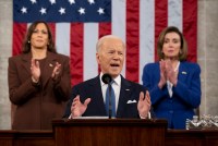President Joe Biden speaks from a podium with Vice President Kamala Harris and House Speaker Nancy Pelosi standing behind him.