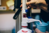 A dispenser pours a dose of methadone — a red liquid — into a plastic cup.