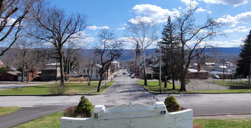 A view of Lewistown, Pennsylvania shows wide roads, buildings, a church and, in the distance, mountains.