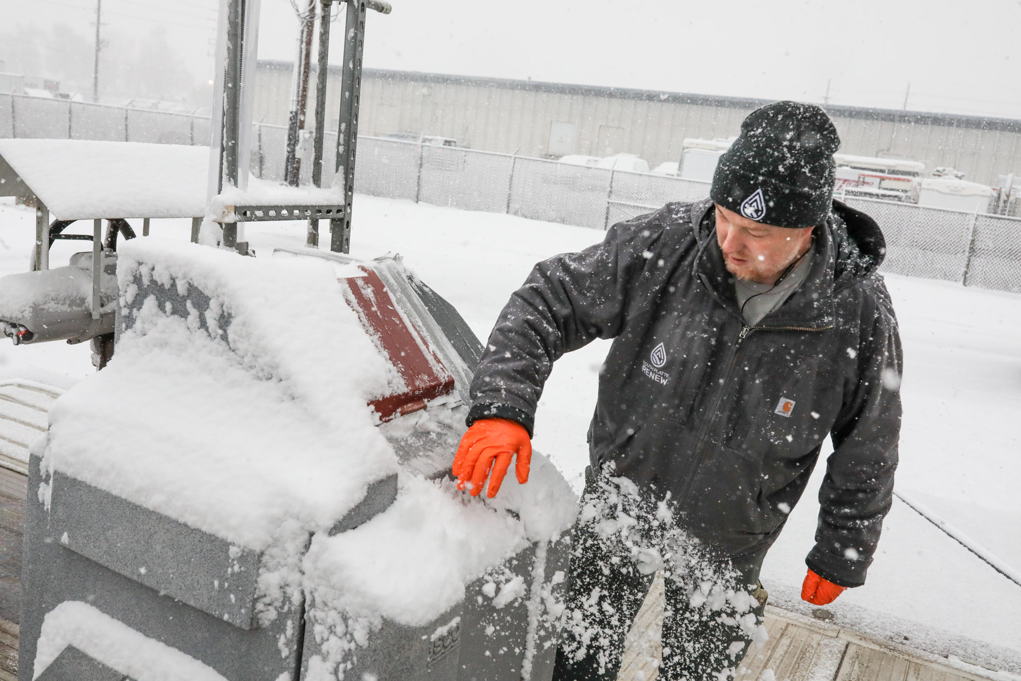 Brandon Hinkhouse is seen standing near a machine, wearing a thick winter jacket, hat and gloves.