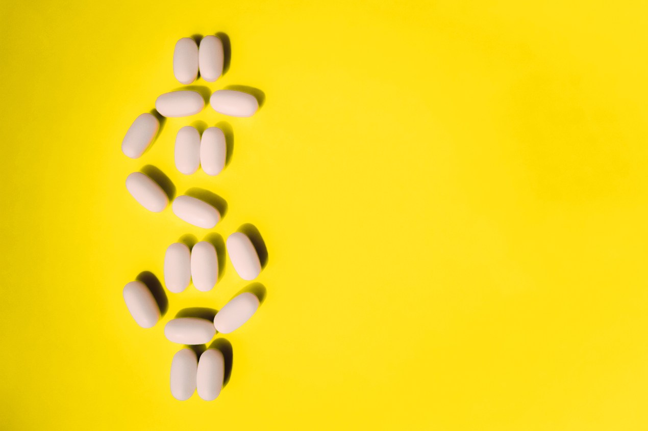 A photo shows pills arranged in the shape of a dollar sign on a bright yellow surface.