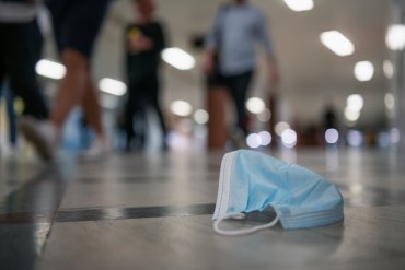 A surgical mask on the floor as many people walk past it.