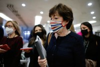Sen. Susan Collins holds a binder and papers while walking. She is wearing a striped mask.