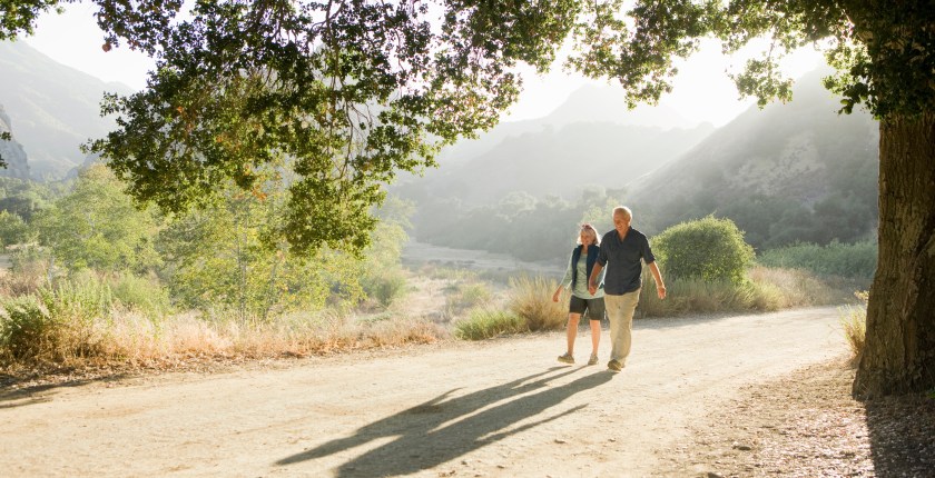 An elderly couple walk on a trail holding hands.