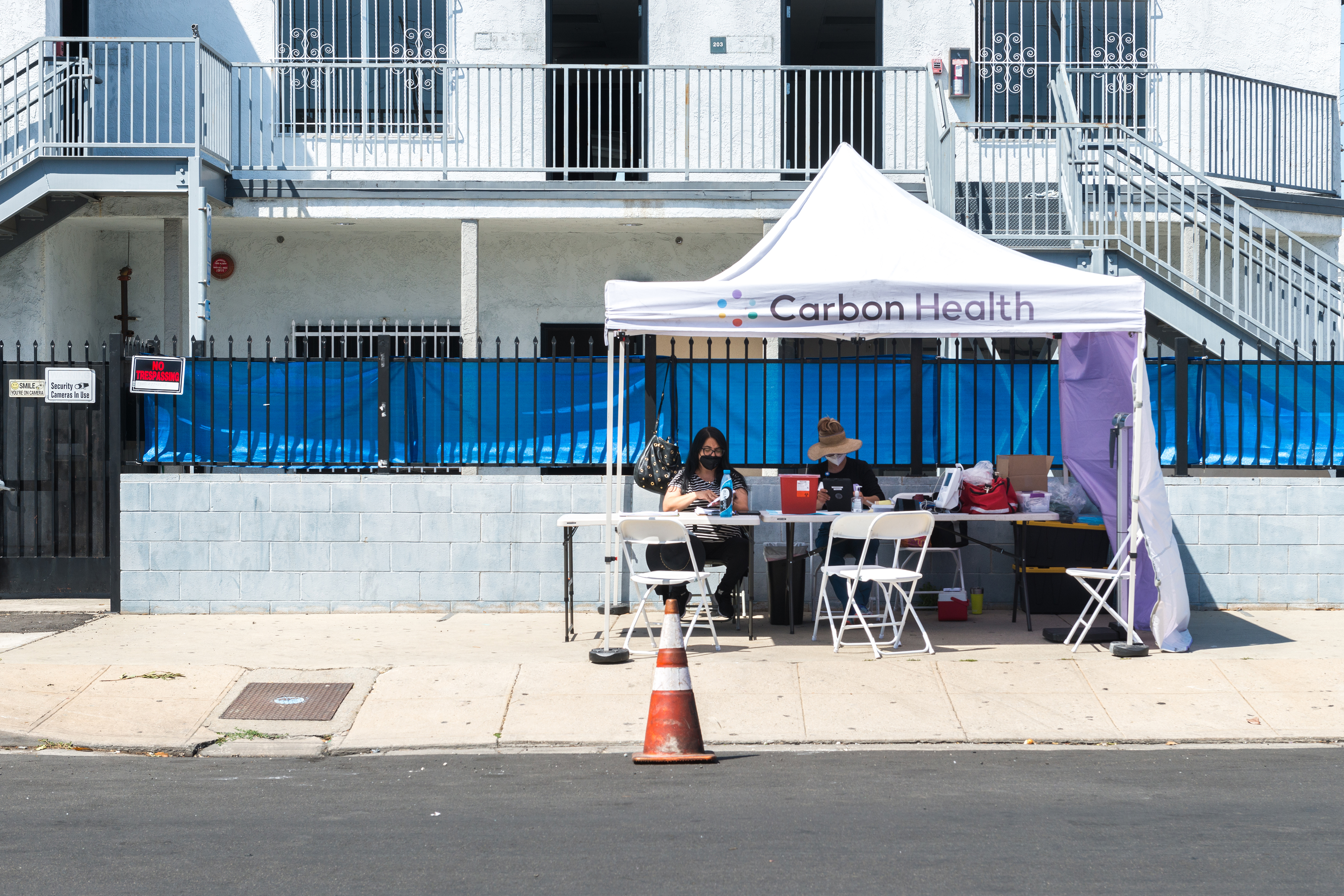 A photo showing a vaccination tent with empty chairs. Two workers sit behind a table in the tent, waiting for people to arrive.