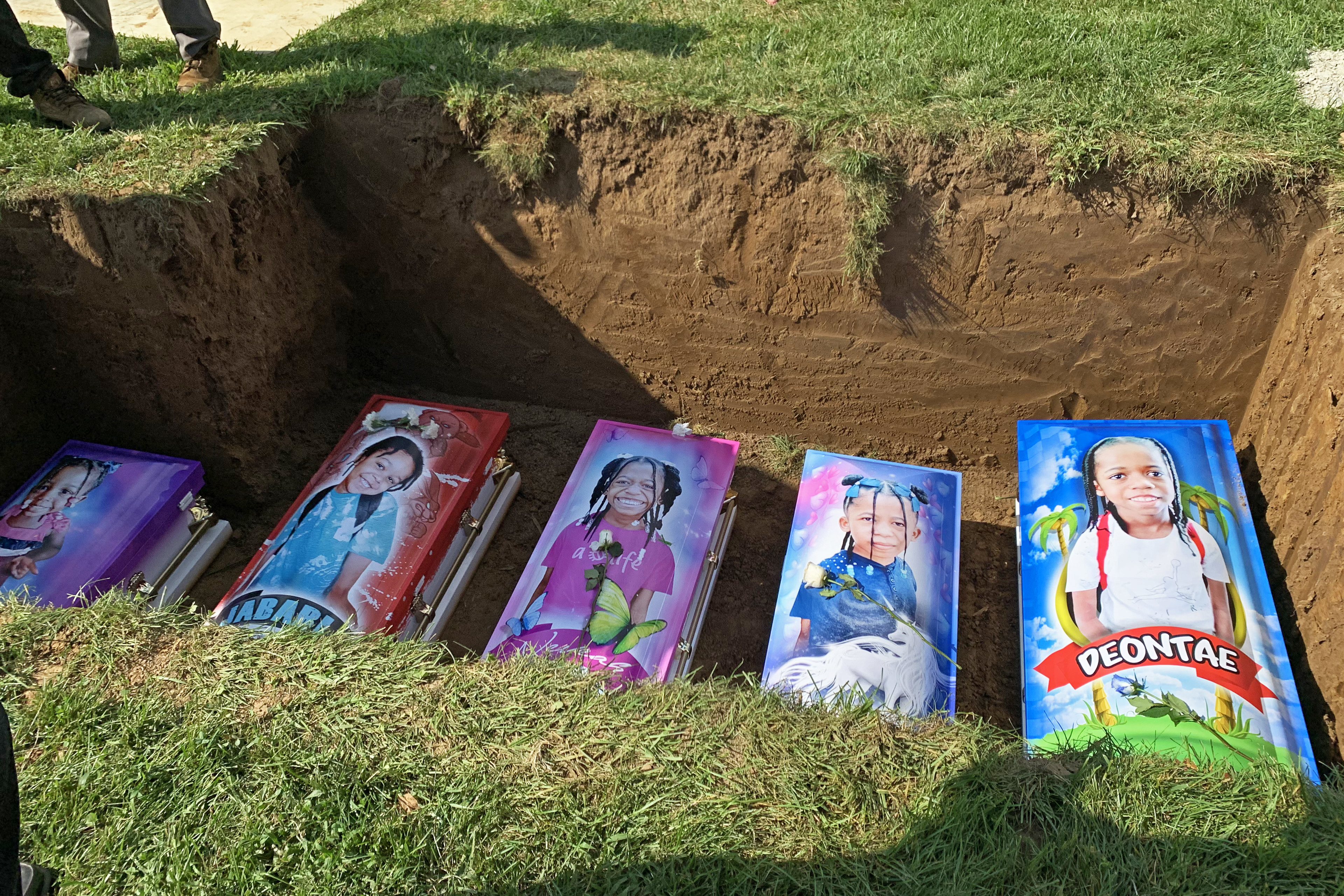 The caskets of five children lay in the ground, printed with images of themselves and bright colors.