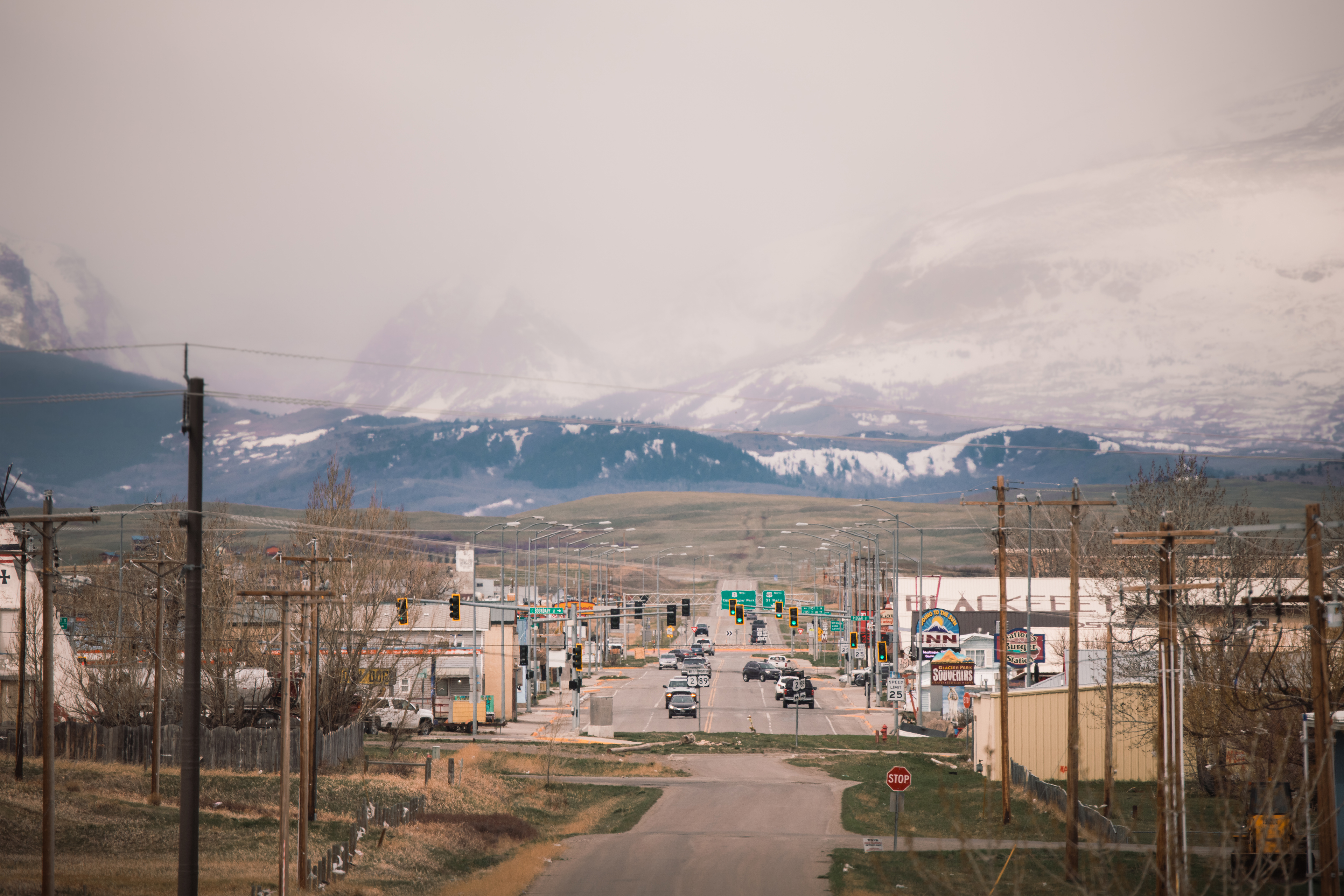 A landscape photo shows a road in Browning, Montana with mountains towering behind it in the background.