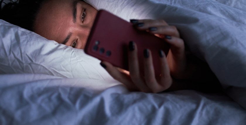 A woman looks at her phone while lying in bed.