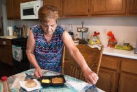 A photo shows Frances De Los Santos in her kitchen peeling off the wrapper of a prepared meal in a frozen food tray. The meal was delivered to her home thanks to a new Medi-Cal program.