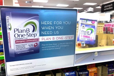 A photo shows an advertisement for Plan B inside of a pharmacy. Text on the sign reads, "Here for you when you need us. Plan B One-Step."