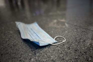 A close up photo shows a surgical face mask discarded on the ground.