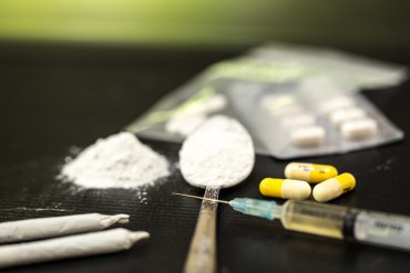 A photo shows a syringe and an array of illegal drugs.