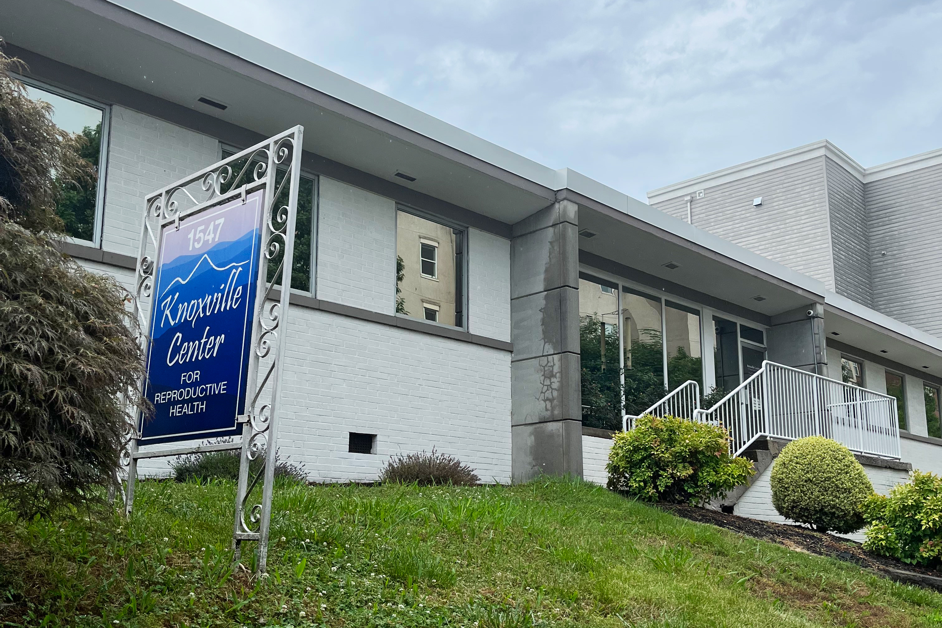 A photo shows the exterior of the Knoxville Center for Reproductive Health. A blue sign to the left of the entryway bears the name of the clinic.