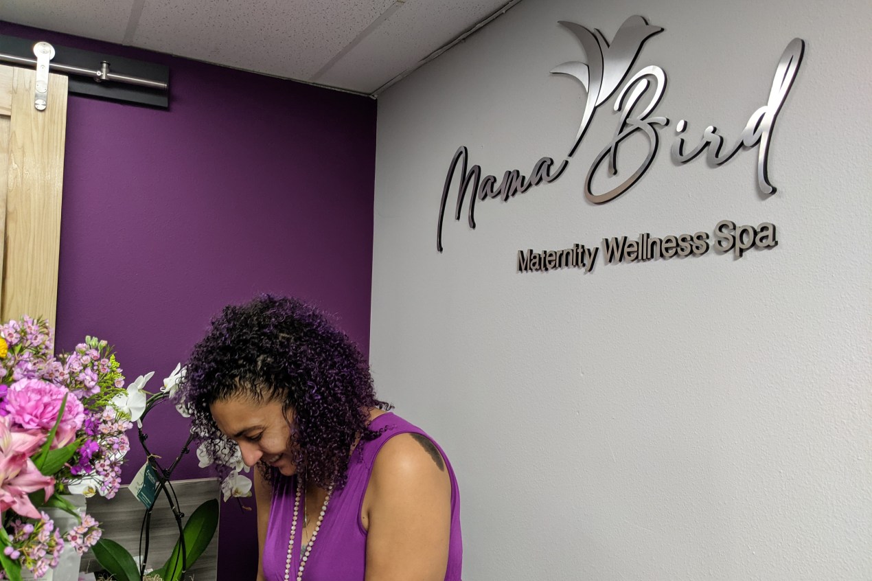 Birdie is seen standing in front of a sign in her spa that reads, "Mama Bird Maternity Wellness Spa."
