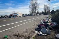 A photo shows a roadway lined with trash and debris. Four RVs are seen parked on the side of the road.