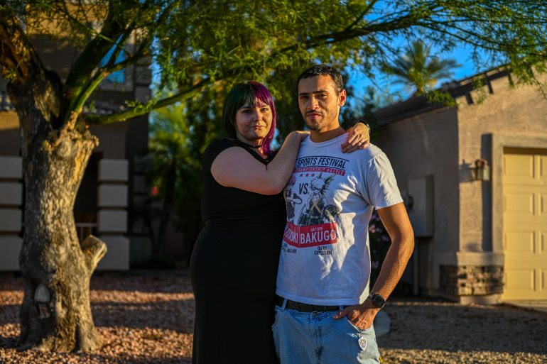 A woman stands with her arms around her husband.