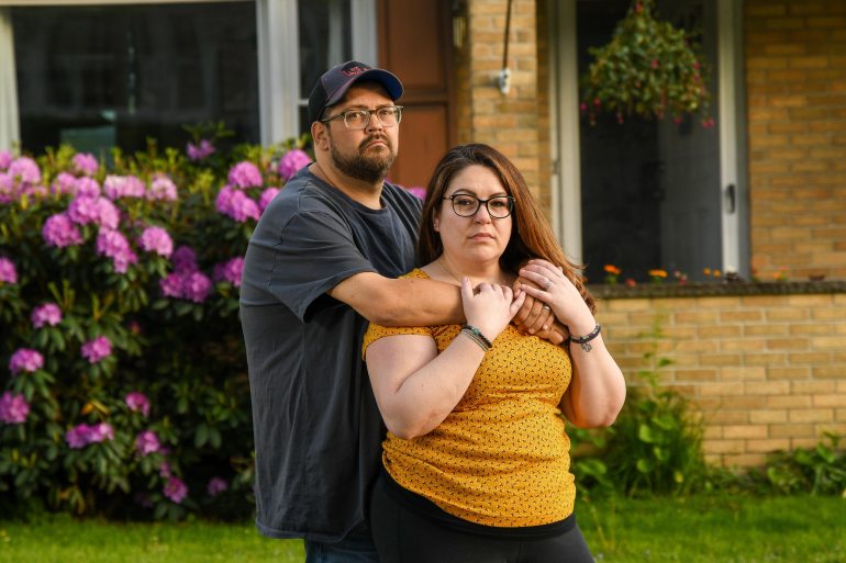 A couple stands together outside their home in Binghamton, NY.