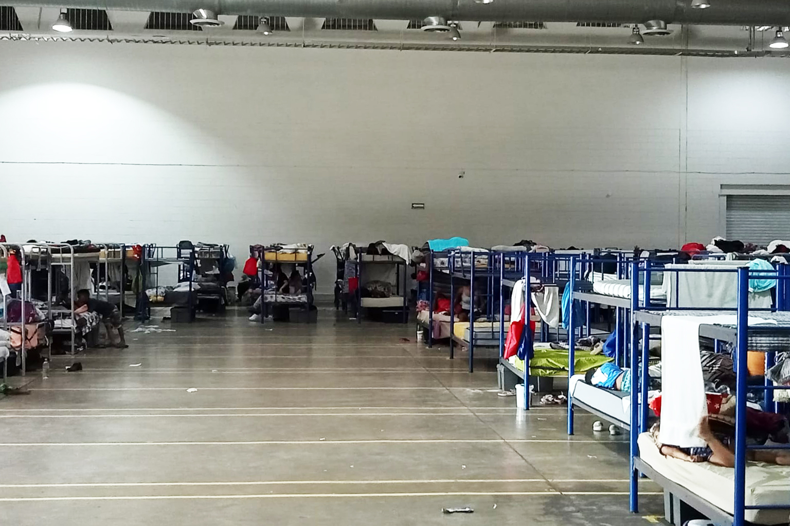 A photo shows the interior of the Leona Vicario shelter. Bunk beds with mattresses are arranged on a repurposed factory floor.