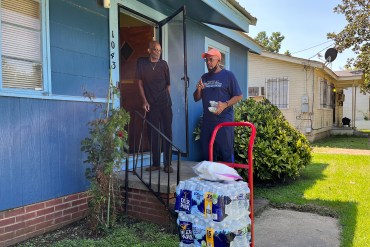 A photo shows Howard Sanders delivering bottles of water to a man at his home.