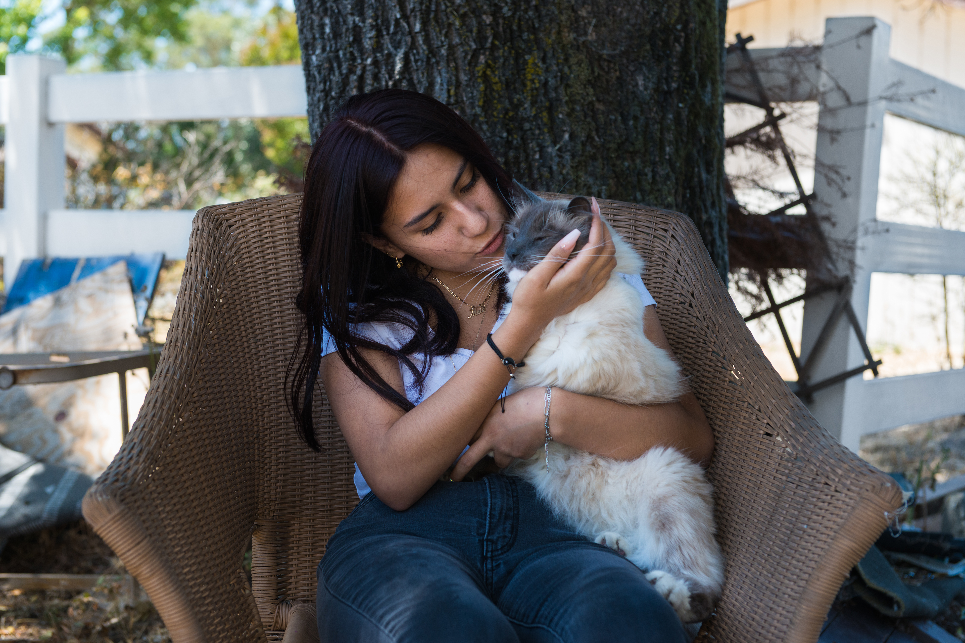 A photo shows Maia Bravo sitting in a chair outside and holding her cat, Misi.