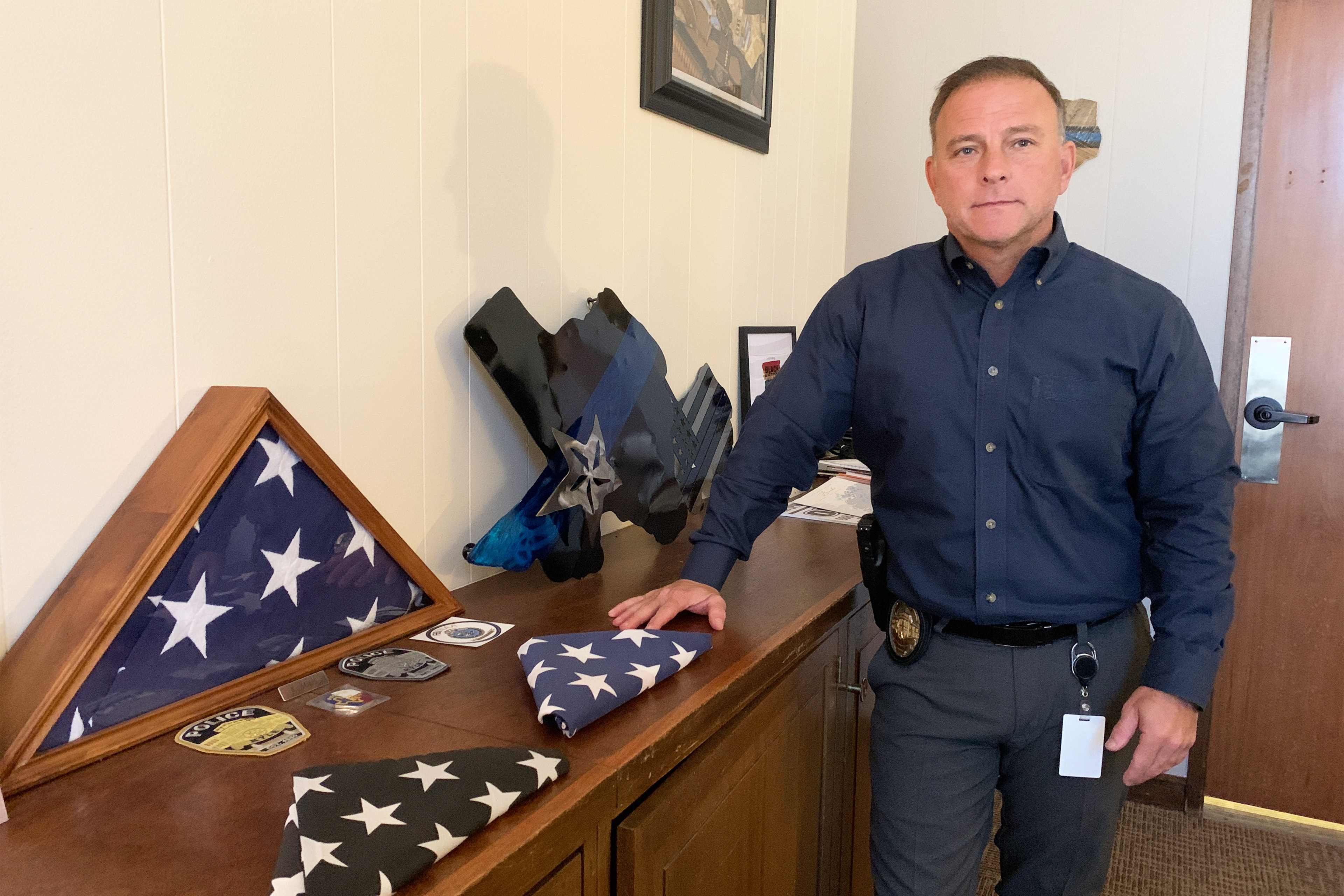 A photo shows Jeff Barnett standing indoors next to several folded American flags.