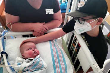 A photo shows Bennett Markow looking at his brother, Eli, in a hospital bed during a family visit.