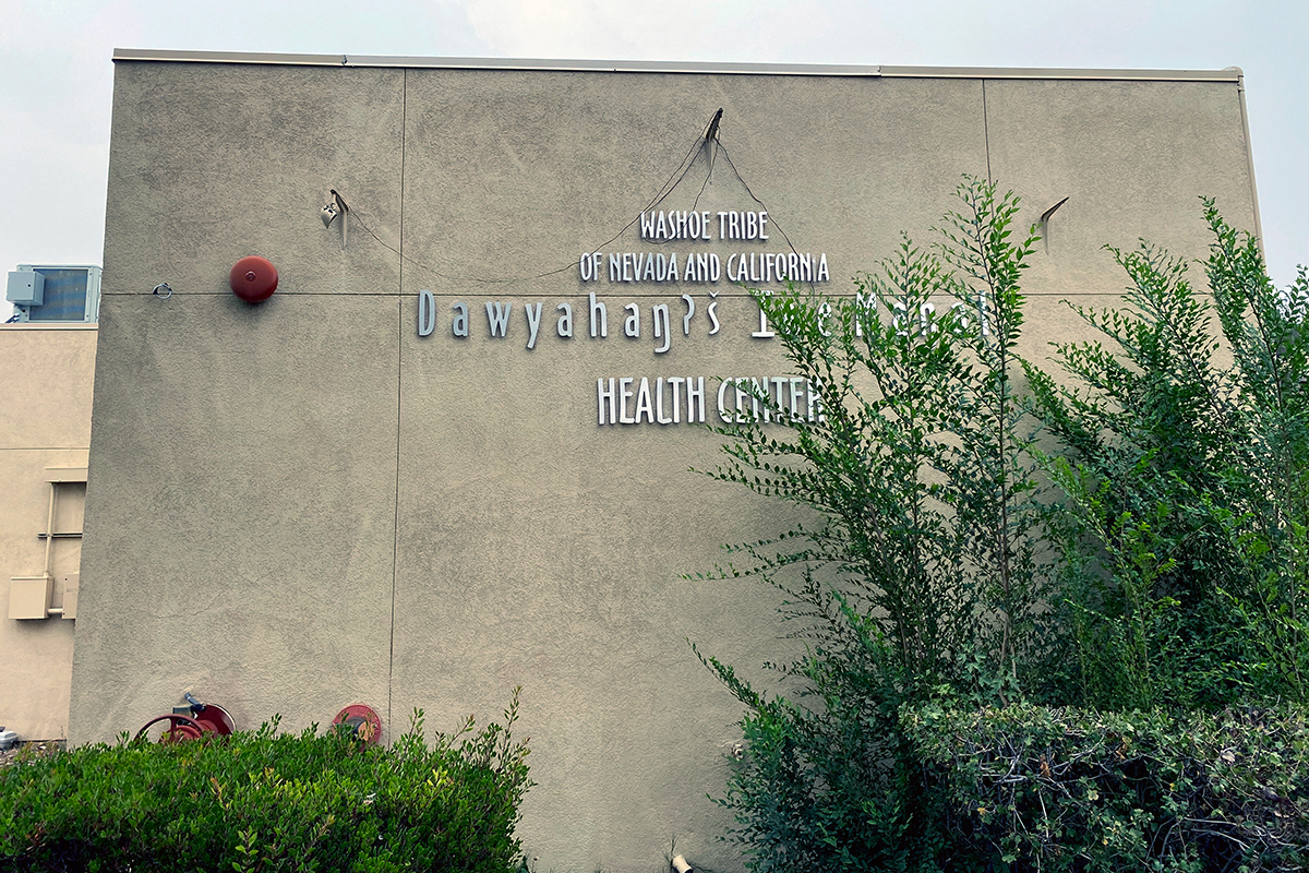 A photo shows the exterior of the Washoe Tribe's health center. Hedges line the exterior.