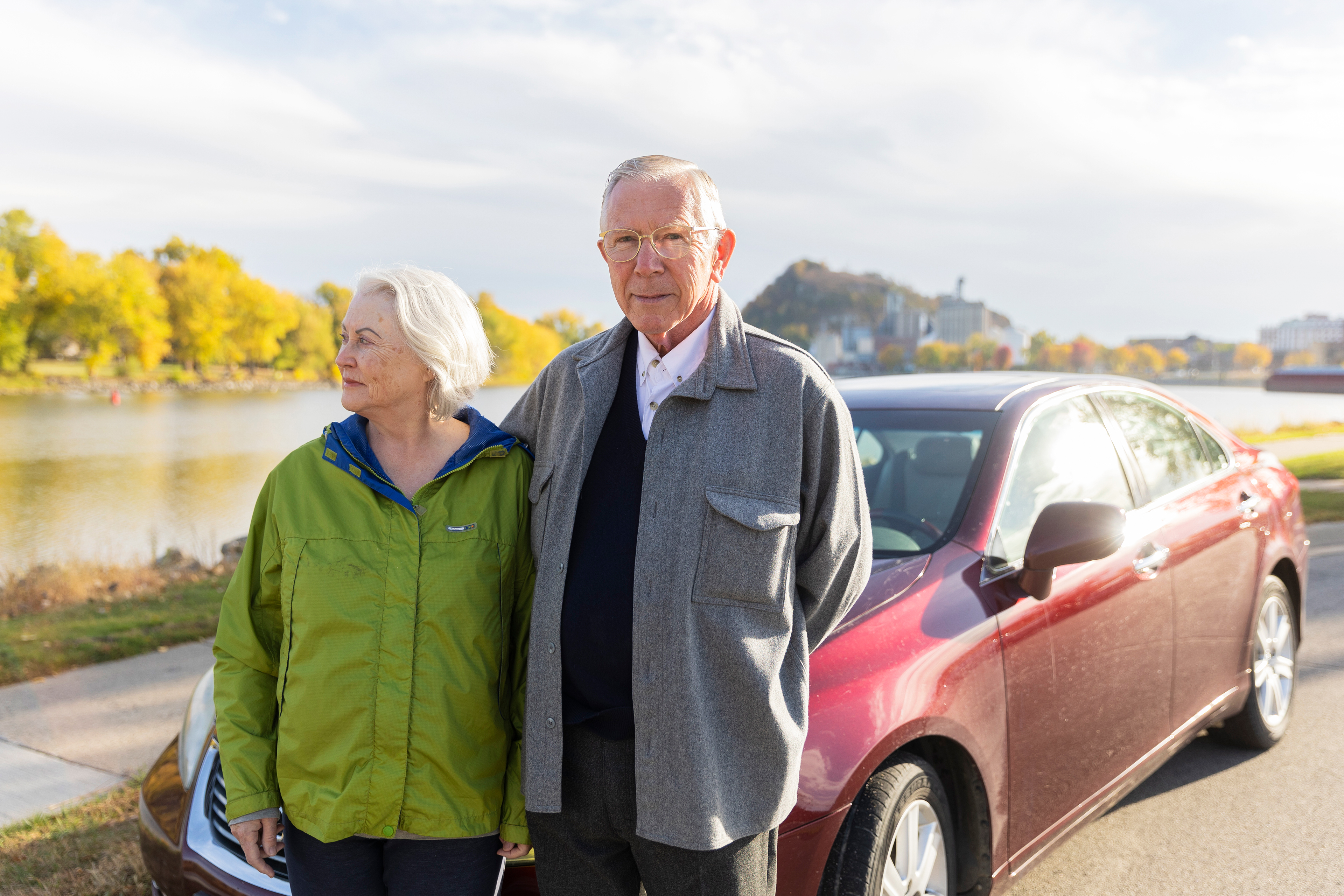 A photo shows Jim and Judie Maybach standing together outside by their car. The city of Red Wing, Minnesota, is seen behind them.