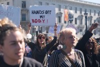 A photo shows a crowd of female protesters. One holds a sign that reads, "Hands off my body."