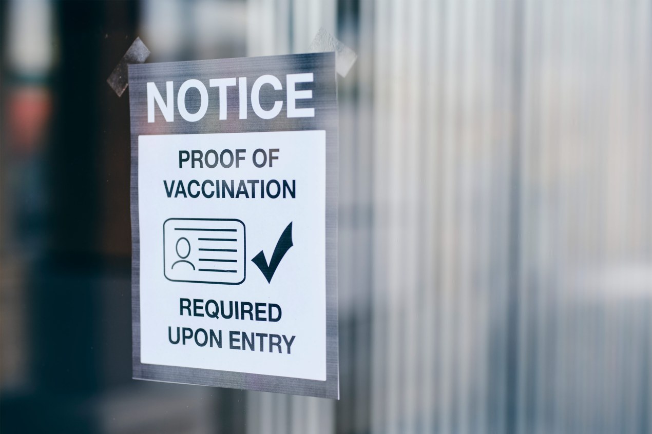 A photo shows a sign on a window that reads, "Note: Proof of vaccination required upon entry."